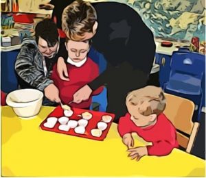 A boy sits with a cupcake baking try in front of him. Two adults cooperate around him to put cake mixture into the tray.