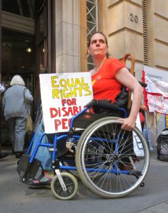 A DPAC wheelchair user at the Dept for Education holds a placard on her lap which reads "Equal rights for disabled people".