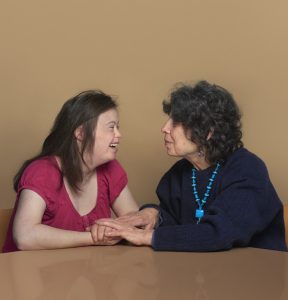 Young woman with Down Syndrome and her mother. They are smiling at each other.