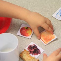 Child's hand with some cards with pictures of food on, and some actual food