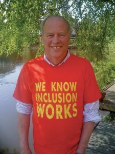 Joe Whittaker smiling at the camera, wearing an ALLFIE t-shirt with the slogan "We know inclusion works"