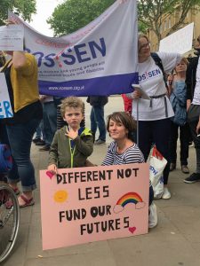 Woman and young child with placard saying "different not less, fund our futures"
