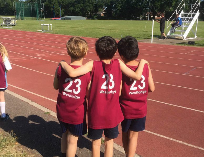 Three small boys with their arms round each other on an athletics track, backs to the camera
