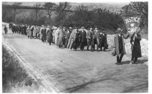 Old black and white photo of a long line of marchers winding through the countryside