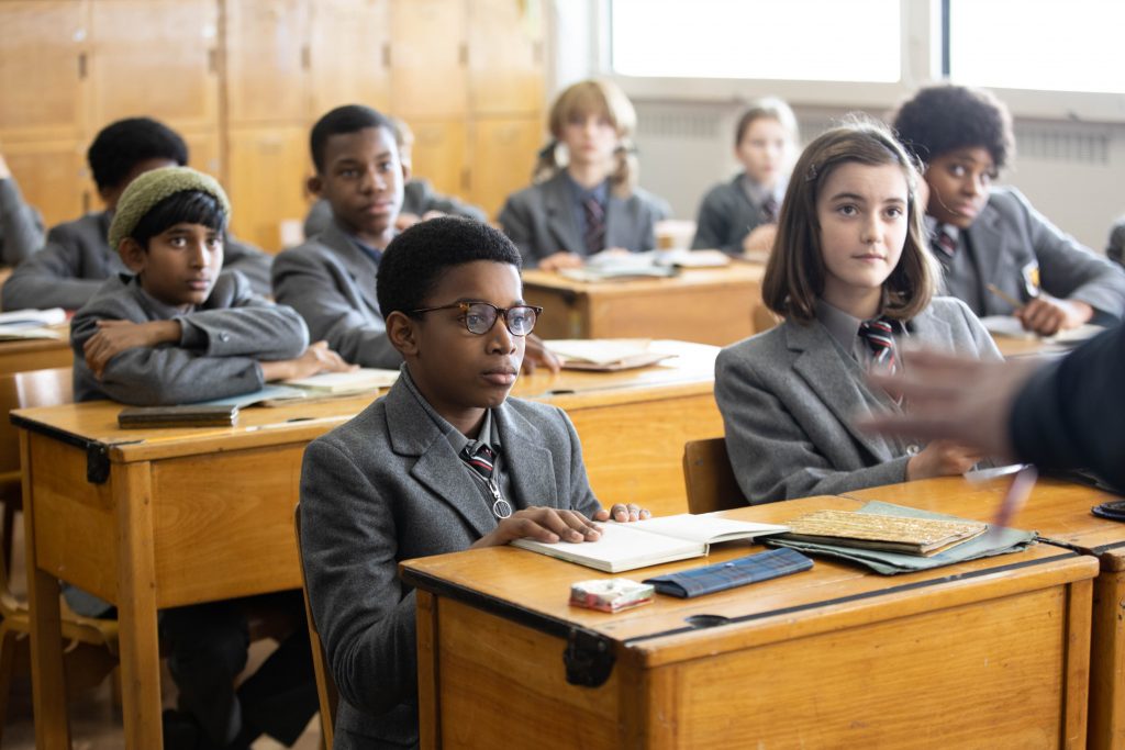 Scene from the BBC film, 'Small Axe: Education' by director Steve McQueen, depicting characters sat at desks in a school classroom setting, with main character Kingsley centre of shot. Education, from the Small Axe season, stars Kenyah Sandy as 12-year-old Kingsley, Ryan Masher as Joseph and Nigel Boyle as Mr Hamley. Copyright: BBC/McQueen Limited.