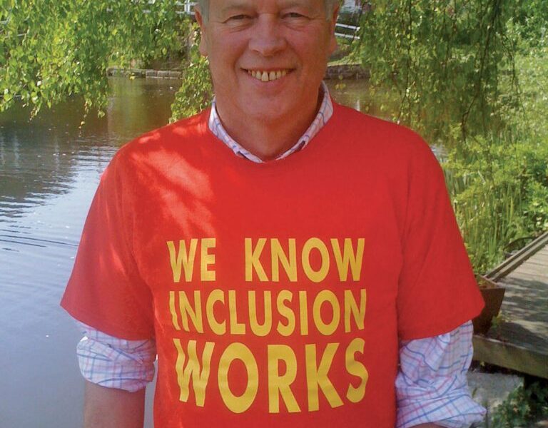 Photograph of Joe Whittaker, smiling to camera and wearing a red shirt with the slogan: 'We Know Inclusion Works'