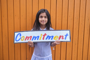 Monega Primary School 6, pupil holding a sign with the text 'Commitment'. Copyright: Monega Primary School