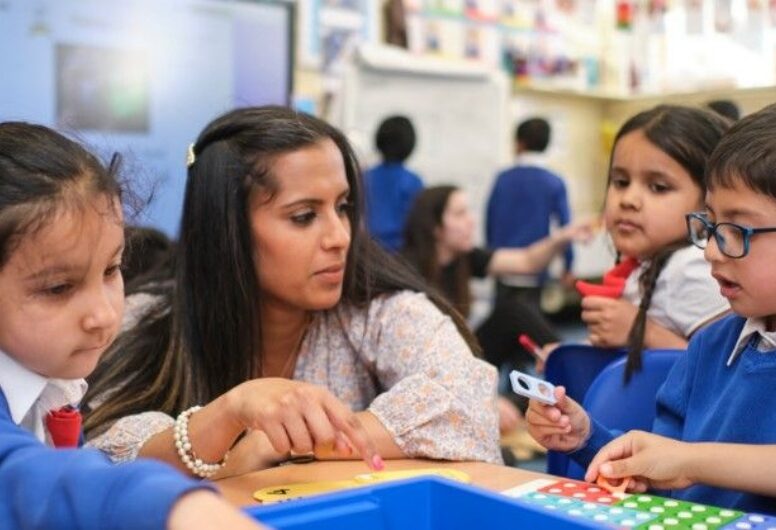 Photograph of puplis learning at Monega Primary School in the London Borough of Newham. Action shot of three pupils in uniform and a Teacher. Copyright: Monega Primary School